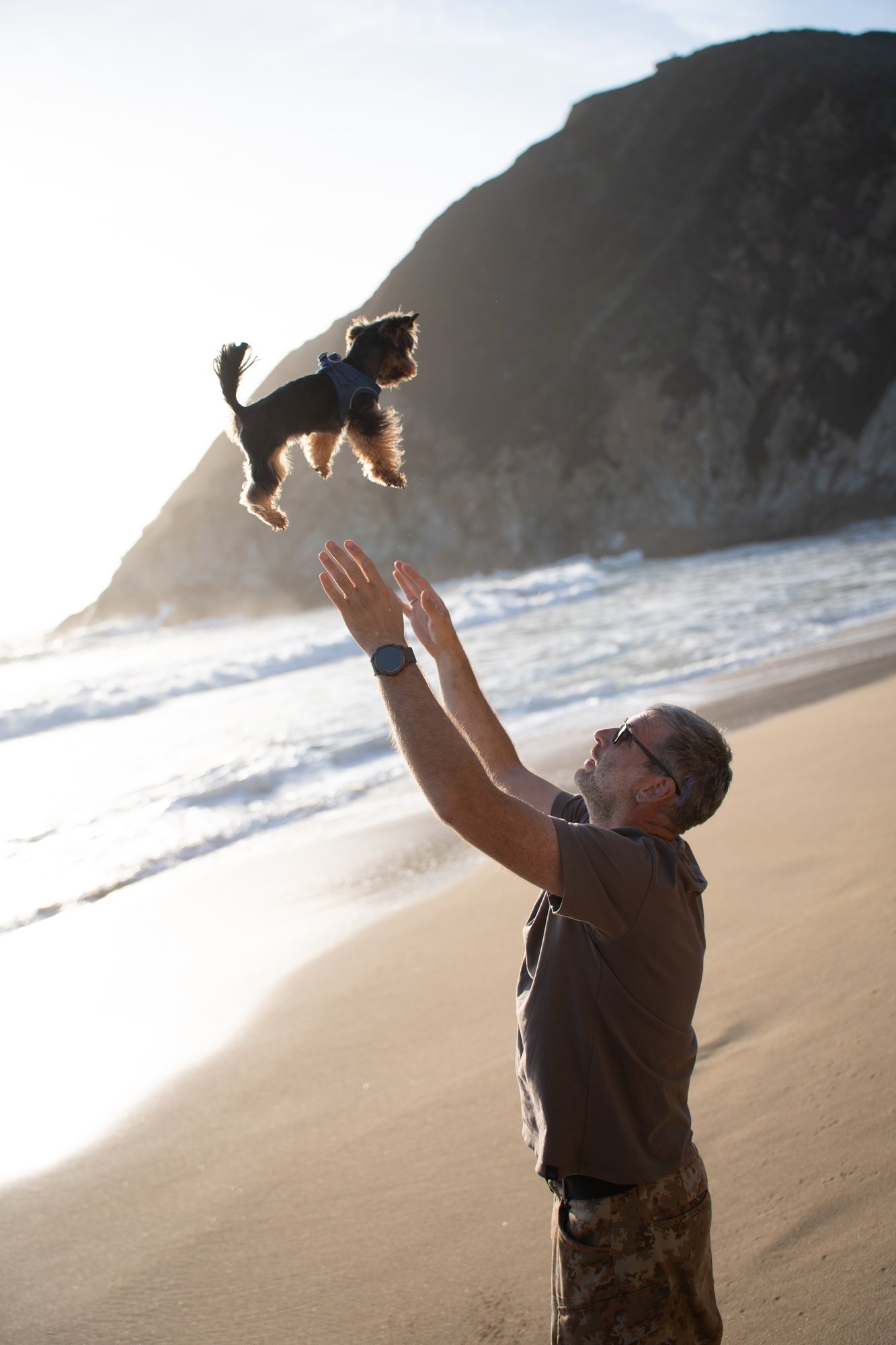 A man holding their dog up beside the ocean