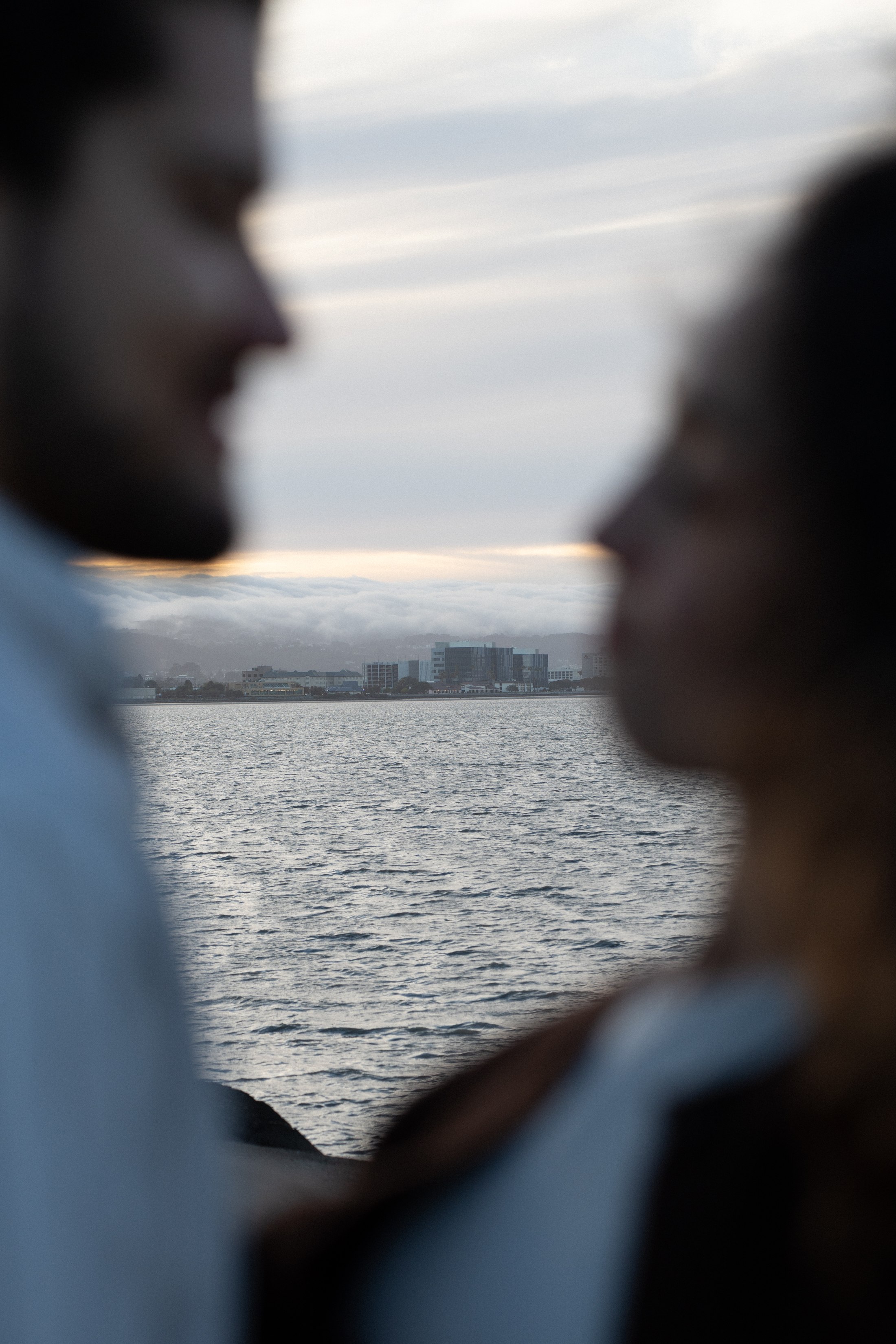A couple softly out of focus beside the bay, with evening light over the water