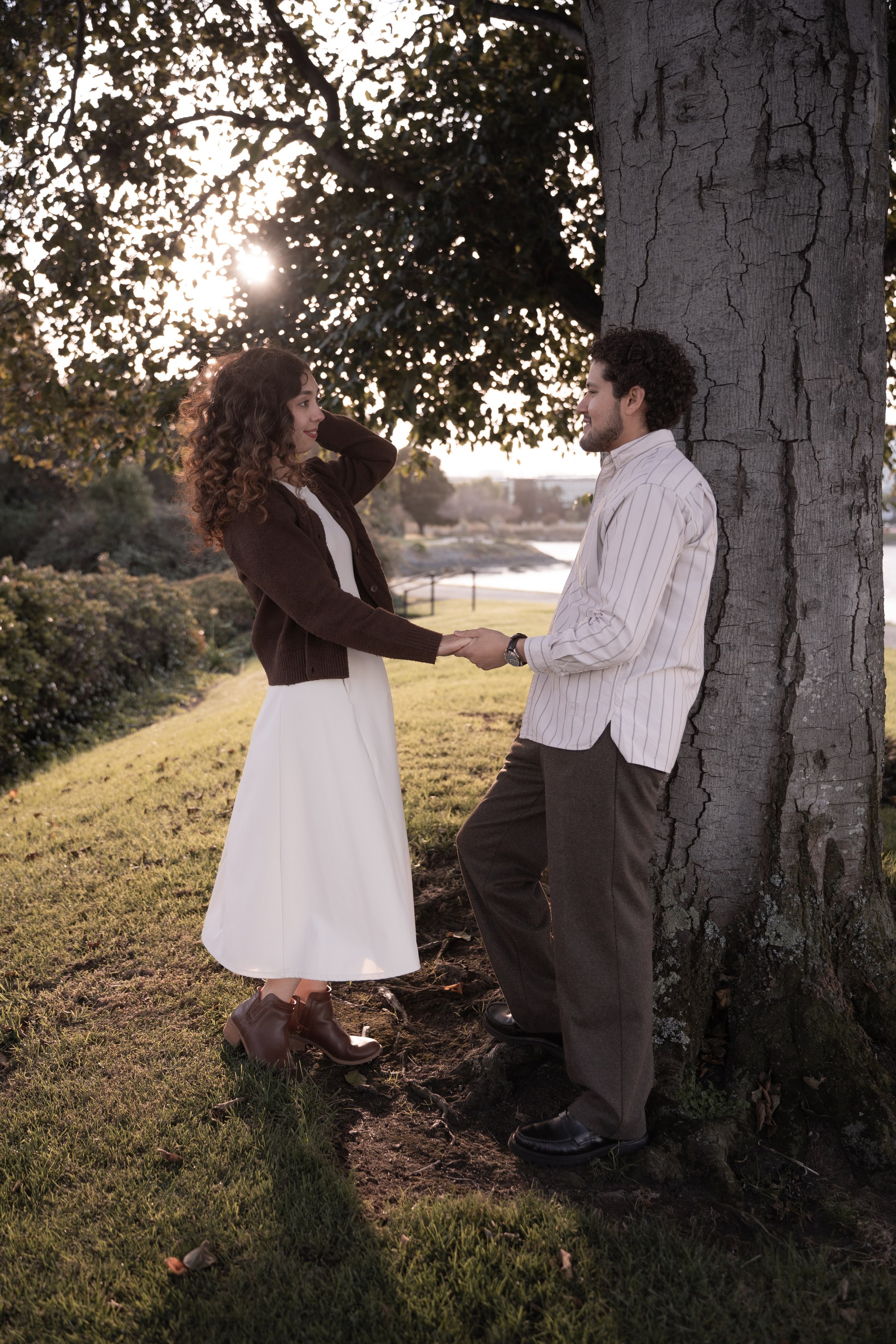 The couple standing together beneath a tree in evening light