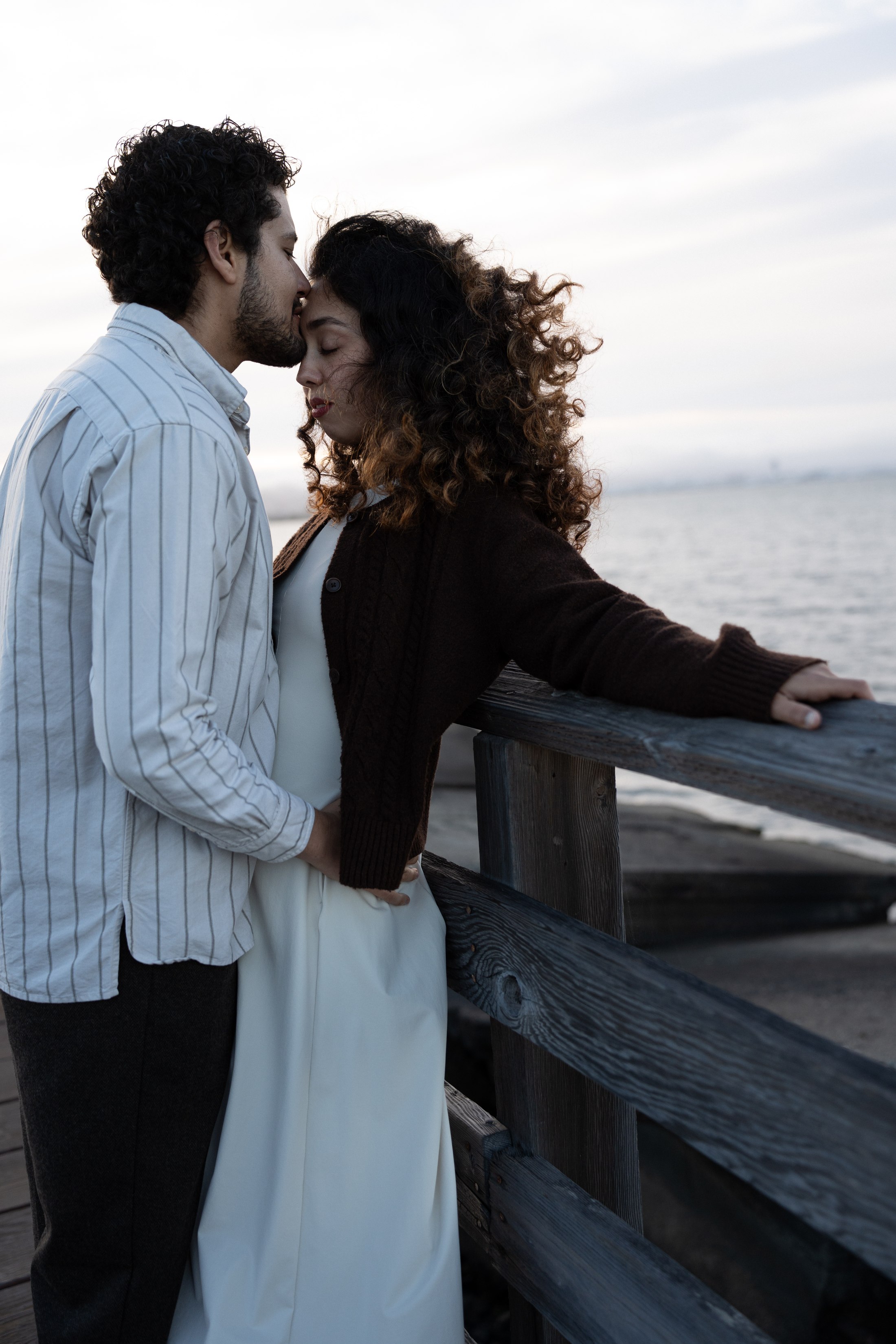 The couple leaning close together against the waterfront railing