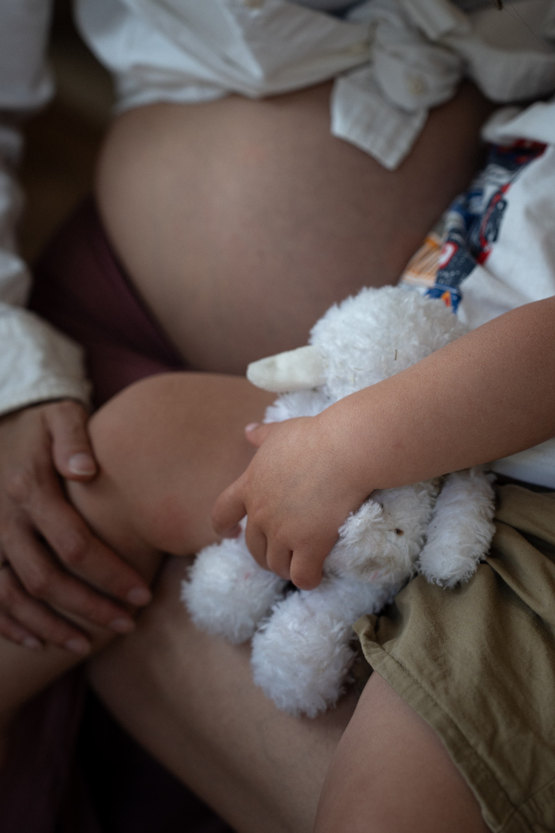 The child holds a small stuffed bunny against his mother’s belly