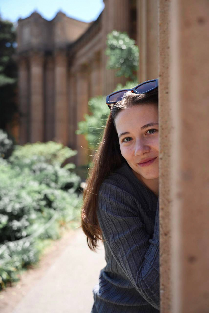 A close portrait of a woman peeking around a stone column